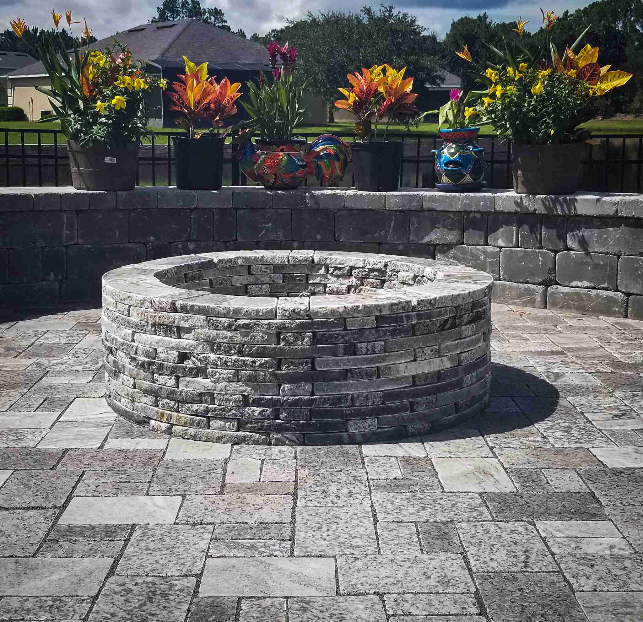 Stacked stone fire pit with retaining wall and colorful planters