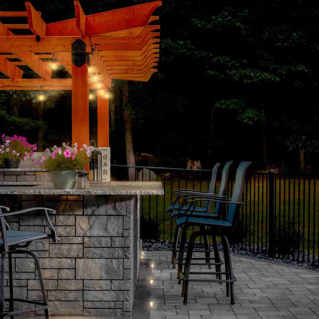 Outdoor kitchen bar with pergola and paver floor lighting